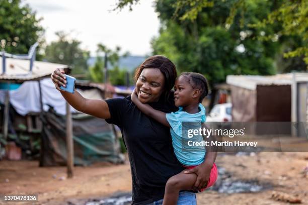 black african lesbian woman holding her cute daughter taking a selfie in an informal settlement - rural africa family stock-fotos und bilder