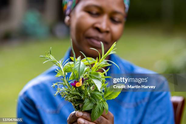 close-up.black african woman holding a bunch of fresh herbs and edible flowers - accompagnement professionnel photos et images de collection