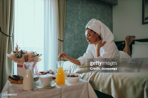 young woman eating breakfast in bed in a hotel room - luxury home dining table people lifestyle photography people stock pictures, royalty-free photos & images