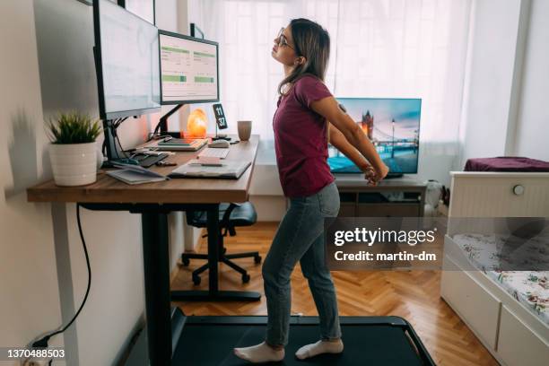 woman at home office is walking on under desk treadmill - woman standing exercise stockfoto's en -beelden