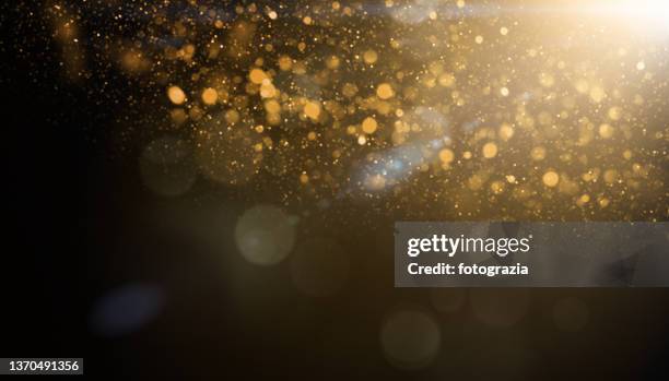 defocused golden glittery particles against dark background with lens flare. christmas overlay - lens flare circle stock pictures, royalty-free photos & images