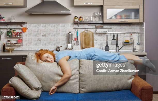 exhausted redhead woman lying on the back of the couch in a loft open space apartment - photography studios stockfoto's en -beelden