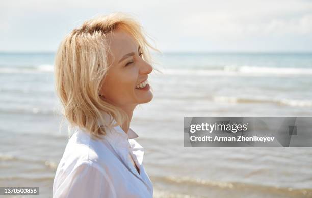 beautiful blond woman wearing white shirt and having fun next to the sea - mujer feliz sola 30 35 fotografías e imágenes de stock