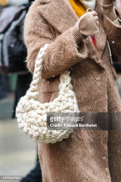 Guest wears a white latte ribbed hoodie pullover, a brown fluffy long coat, braided macrame braided shoulder bag, beige mittens / gloves, a yellow...
