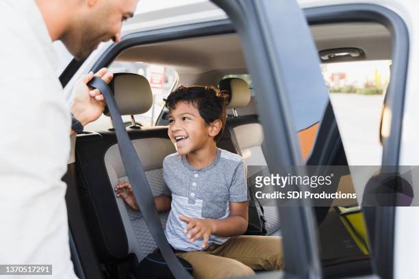 mid adult dad helps young son buckle into car seat - happy arab family on travel stock pictures, royalty-free photos & images