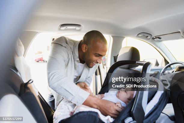 new dad puts baby girl in safety seat in car - car seat stock pictures, royalty-free photos & images
