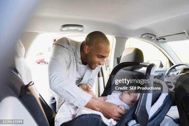 new dad puts baby girl in safety seat in car - car safety stock pictures, royalty-free photos & images