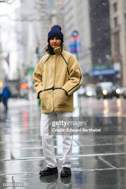 Guest wears a navy blue ribbed wool beanie, a yellow sheep with black leather straps coat, white denim cargo pants, black shiny leather ankle boots,...