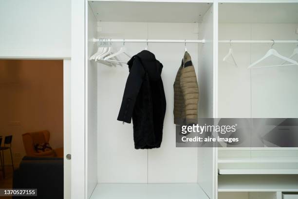 close-up of a white wardrobe with two jacket garments hanging on hangers next to several empty white hangers - abrigo blanco artículo de moda fotografías e imágenes de stock