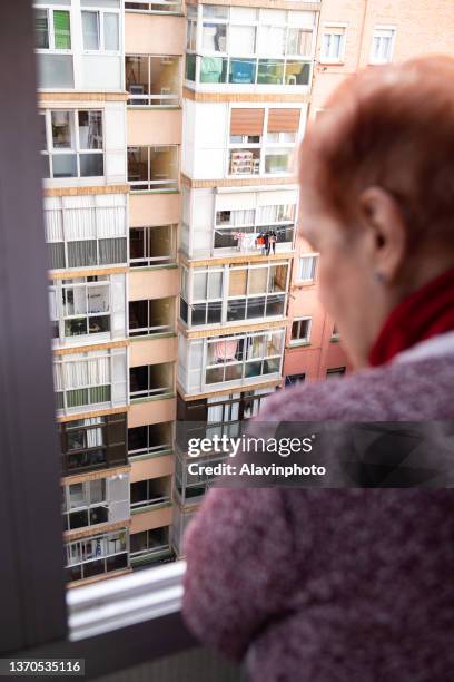 old woman leaning out the window of a high floor in the city in solitude - confusión stock-fotos und bilder