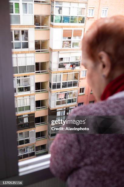 old woman leaning out the window of a high floor in the city in solitude - confusión 個照片及圖片檔