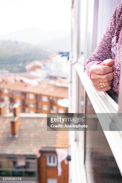 old woman leaning out the window of a high floor in the city in solitude - confusión stock-fotos und bilder