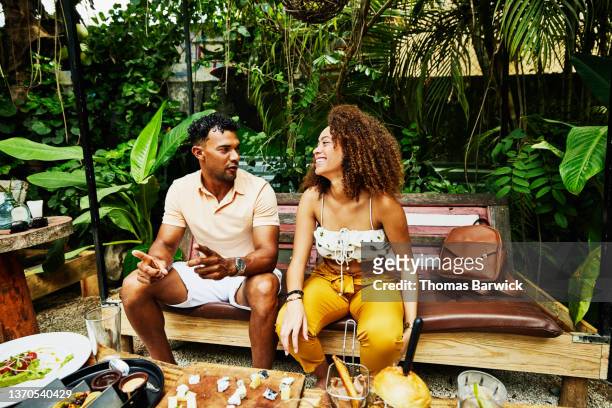 medium wide shot of laughing woman sharing lunch with boyfriend at outdoor cafe - sprechen zusammen cafe stock-fotos und bilder
