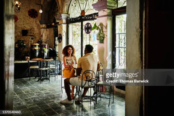 Wide shot of smiling couple in discussion while sharing drinks in cafe
