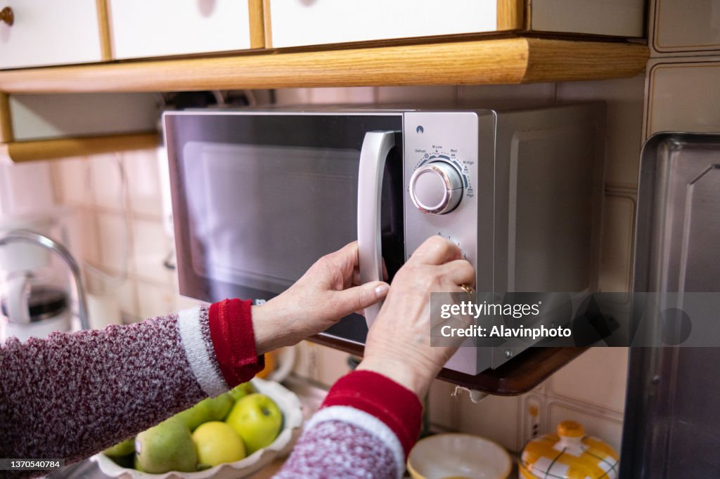 Old woman closing the microwave in her kitchen