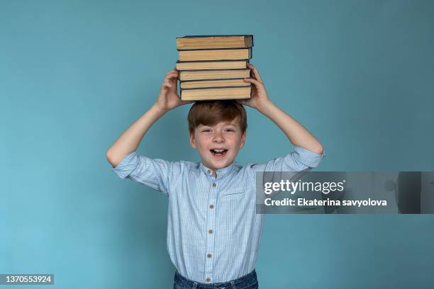 happy little boy with books on his head, isolated on a blue background - fachbuch stock-fotos und bilder