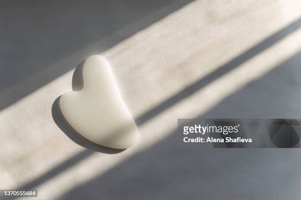 gua sha massager of white color lies on a white background in the sun with hard shadows - spooning stock pictures, royalty-free photos & images