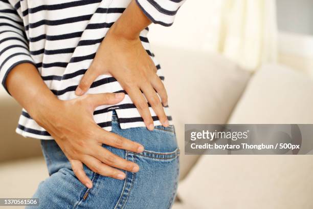 health problems,woman back muscle pain,midsection of woman with stomachache sitting on sofa at home - hip pain stock-fotos und bilder