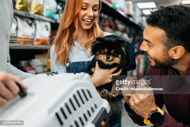 glückliches paar mit ihren welpen, die spielzeug und hundefutter in der zoohandlung kaufen. - service dog stock-fotos und bilder