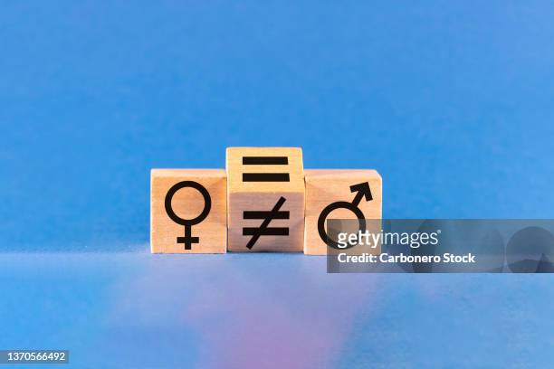 concept of gender equality. wooden block with unequal sign is rotating to change the symbol to equal between two wooden blocks with male and female symbols. studio shot. - loonkloof stockfoto's en -beelden