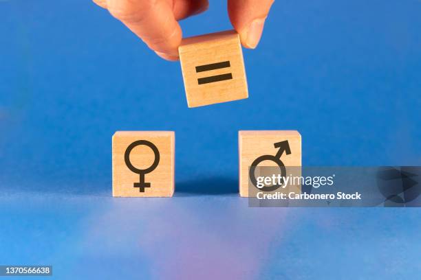 concept of gender equality. one hand places a wooden die with the equal sign between the male and female symbols. - gleichheit stock-fotos und bilder