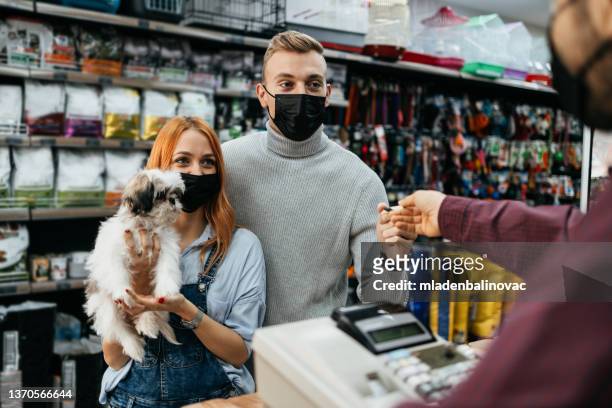 happy couple with their puppies buying toys and dog food in pet shop. - pet shop stock pictures, royalty-free photos & images