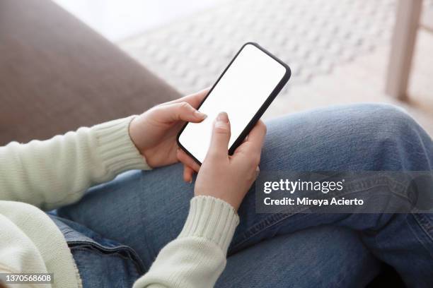 over the shoulder view of a caucasian womans hand, using a cell phone in their home, wearing casual clothing. - hand back lit stock pictures, royalty-free photos & images