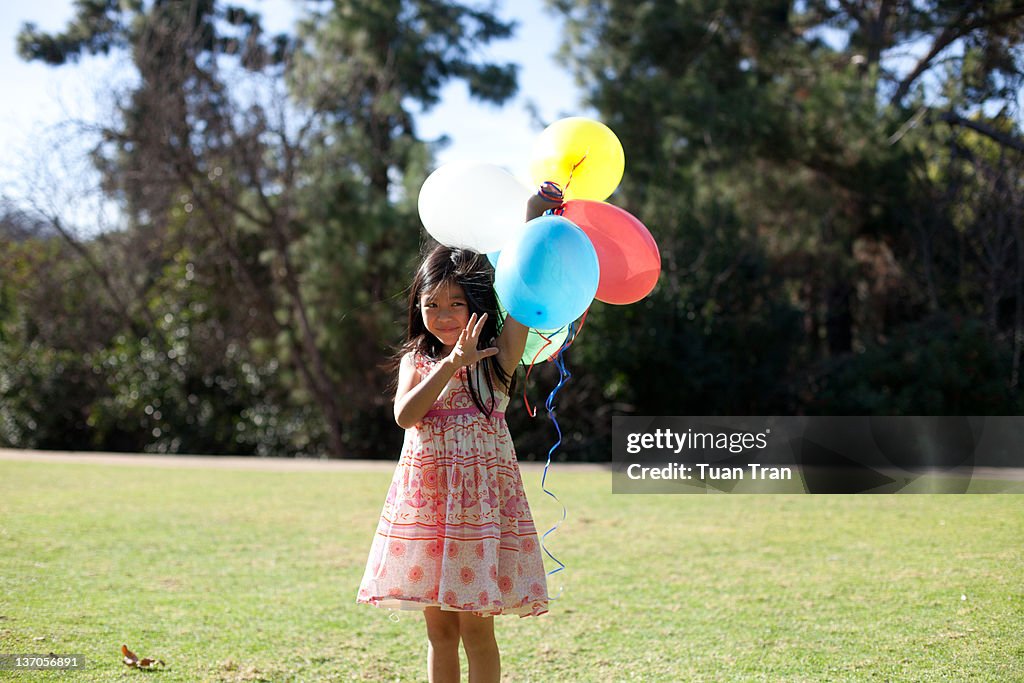 Young girl holding balloons at park