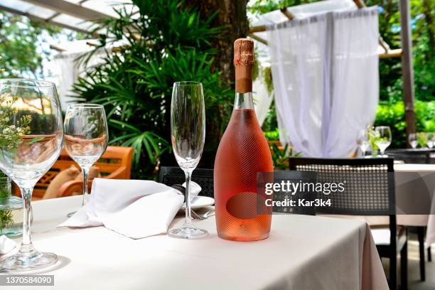 schöne flasche rosé-sekt mit weingläsern auf restauranttisch mit grünem gartenhintergrund - wine rose stock-fotos und bilder