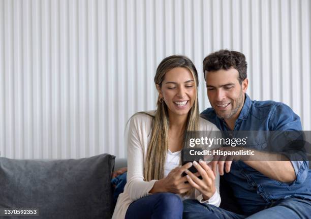 feliz pareja en casa riendo mientras mira las redes sociales - pareja viendo celular fotografías e imágenes de stock