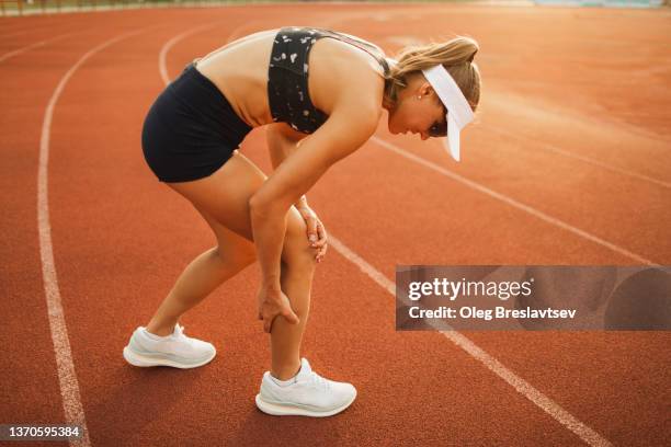 woman hurted ankle on running sports track. spasm and pain, female health problems in professional sports - female muscular calves fotografías e imágenes de stock