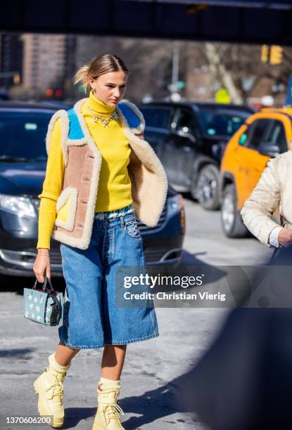 Guest is seen wearing yellow turtleneck, necklace, shearling vest, denim shorts, blue bag, laced yellow boots, socks outside Coach during New York...