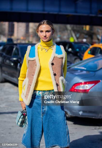 Guest is seen wearing yellow turtleneck, necklace, shearling vest, denim shorts, blue bag, laced yellow boots, socks outside Coach during New York...