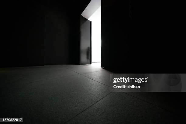 dark room with a door leading to light - dark room stock-fotos und bilder