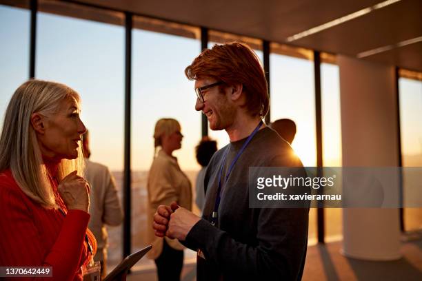 smiling colleagues talking in open office space at sunset - office sunlight stock pictures, royalty-free photos & images