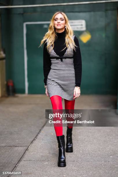 Chiara Ferragni wears silver and large rhinestones pendant earrings, a black turtleneck wool pullover, a black and white checkered print pattern...