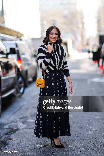 Guest wears a black and white zebra print pattern turtleneck pullover, a yellow shiny leather shoulder bag from Carolina Herrera, black with white...