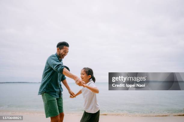 father and young daughter dancing in rain on beach at dusk - father daughter dance stock-fotos und bilder