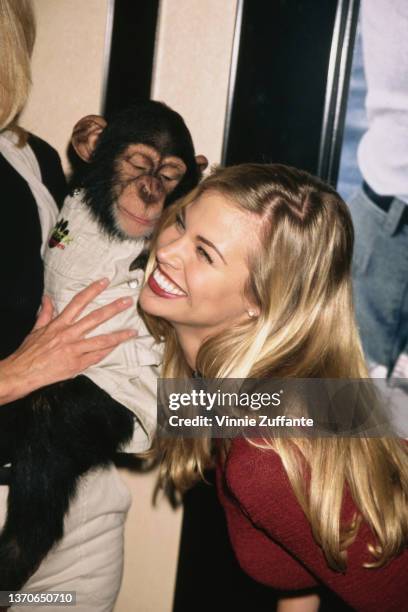 American actress and television personality Brooke Burns poses with a young chimpanzee at the 1996 National Association of Television Program...