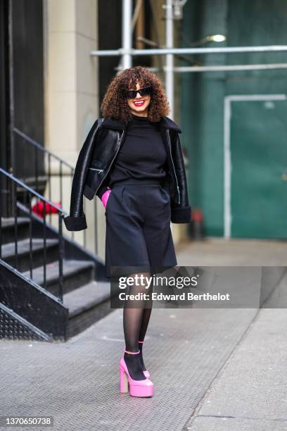 Lena Mahfouf aka Lena Situations wears black sunglasses, a black high neck wool pullover, neon pink tulle gloves, a black shiny leather with sheep...