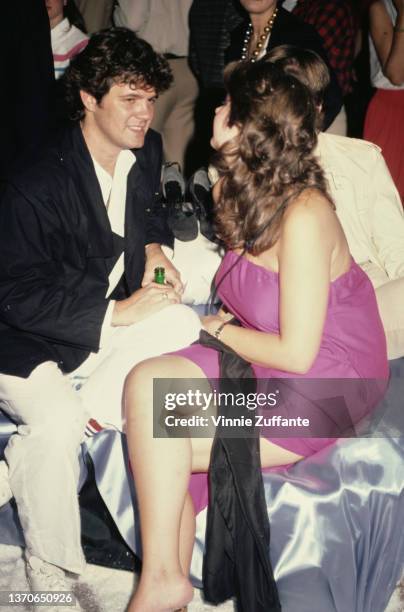 Steve Carson, wearing a black jacket with white trousers and a white shirt, with Maria Burton, wearing a pink strapless dress, attend an event,...