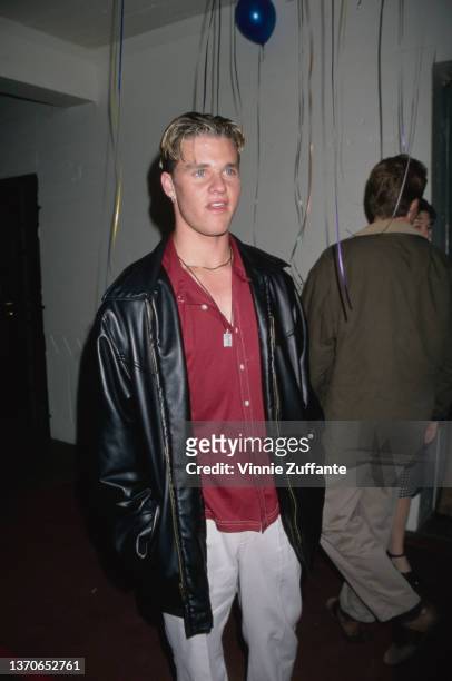 American actor Zachery Ty Bryan, wearing a red shirt beneath a black leather jacket with white trousers, attends an event, 1998.