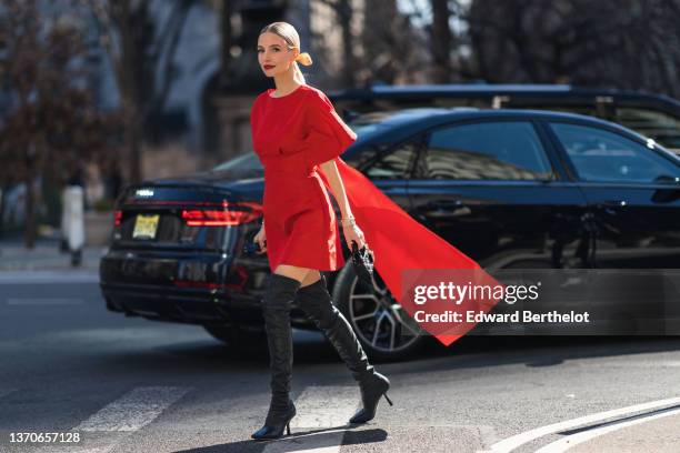 Leonie Hanne wears black sunglasses, gold earrings, a red oversized short sleeves / belted short dress with a large knot train in the back, gold...