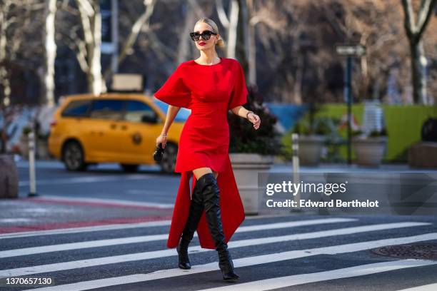 Leonie Hanne wears black sunglasses, gold earrings, a red oversized short sleeves / belted short dress with a large knot train in the back, gold...