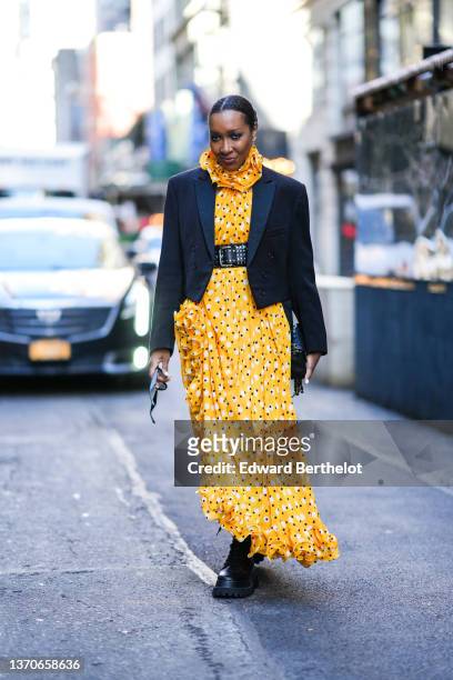 Guest wears silver earrings, a yellow with black and white polka dots print pattern ruffled halter neck / long asymmetric dress, a black shiny...