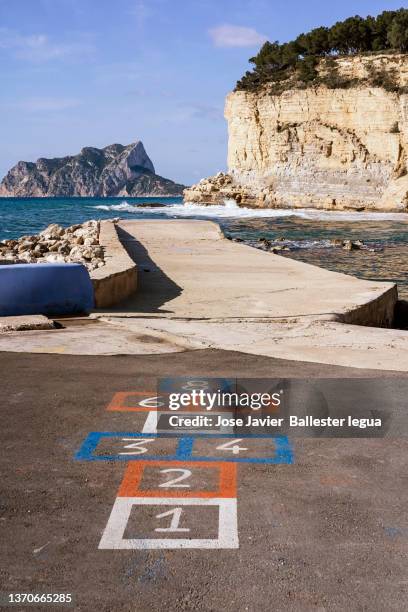 hopscotch game painted in colours on the asphalt overlooking the beautiful landscape of the mediterranean sea on a beautiful sunny day. vertical viewpoint - hopscotch stock pictures, royalty-free photos & images