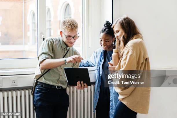 student showing his colleagues something on laptop - friend at work stock-fotos und bilder