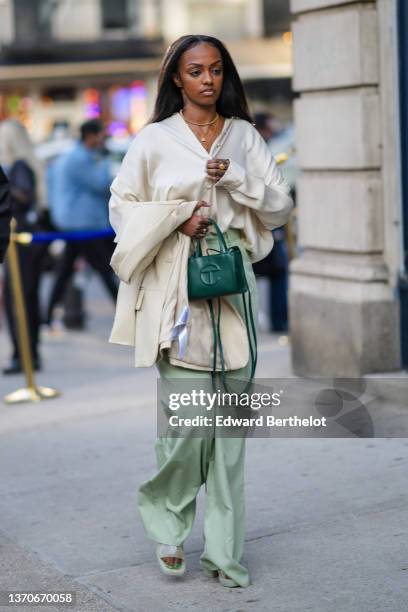 Guest wears gold piercings, gold chain pendant necklaces, a white latte buttoned blouse, a beige blazer jacket, a dark green shiny leather handbag...