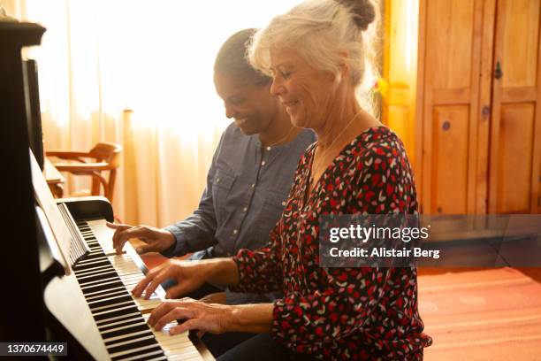 two mature women playing the piano together at home - pianist stock-fotos und bilder