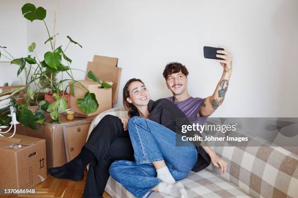 young couple on sofa taking selfie - selfie indoors stock pictures, royalty-free photos & images